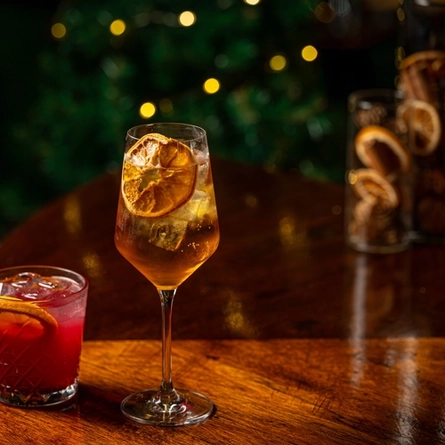 Two cocktail type drinks on a bar.  One in a low ball tumbler and the other is in a stemmed glass.
