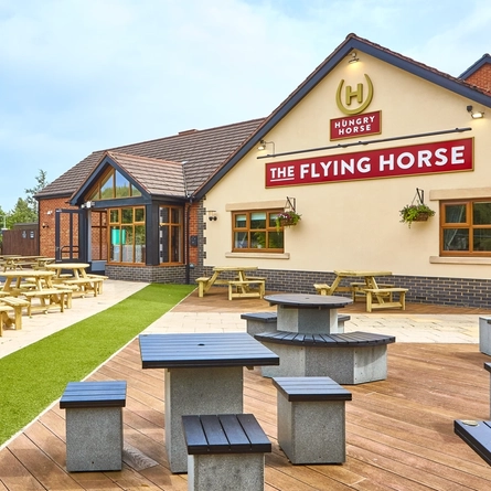 The exterior facade, signage and beer garden seating area with wooden picnic tables and children's play area, at The Flying Horse in Heald Green.