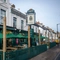 The exterior facade, signage, and seating area of The Grosvenor, with string lights above the wooden picnic tables and shade umbrellas.