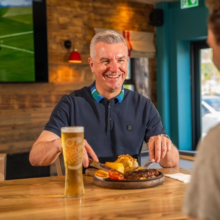 A close up of a father sat in the interior restaurant and seating are eating a main meal of steak smiling on Fathers day at a Flaming Grill venue.