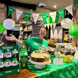 A woman stood behind a bar decorated with Macmillan merchandise.