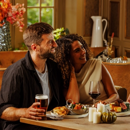 An image of 2 people enjoying 2 Game Night Main dishes and drinks within the interior restaurant and seating area at The Foundry Bell.