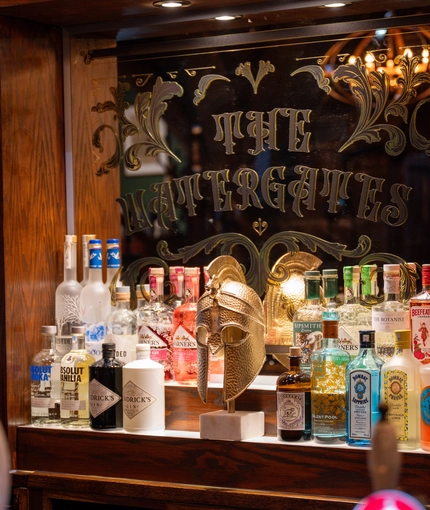 An image of the interior bar focusing on the venue signage displayed on a mirror behind a metallic Roman mask ornament at The Watergates Bar.