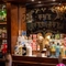 An image of the interior bar focusing on the venue signage displayed on a mirror behind a metallic Roman mask ornament at The Watergates Bar.