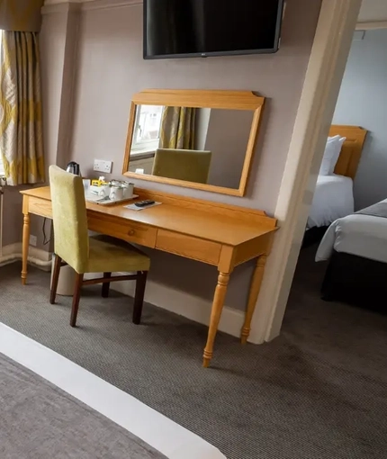 A interior family hotel bedroom with a double bed, two single beds, a dressing table with mirror and a TV at The Commodore.