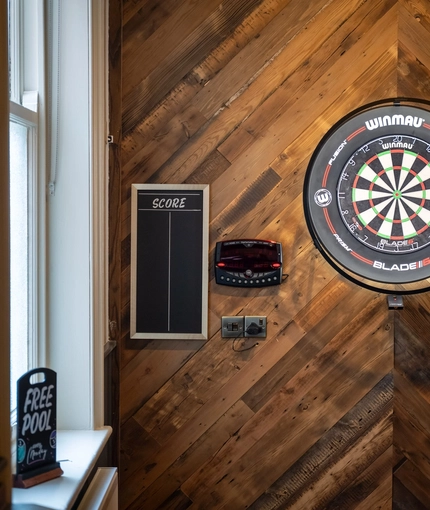 A close up view of the illuminated dartboard on the wall inside The Victoria, with a score board on the wall beside it.
