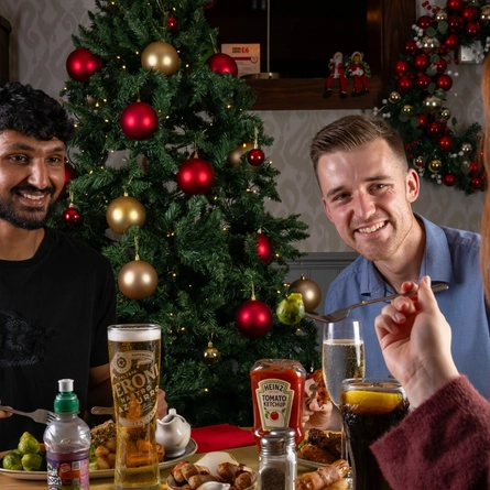A group of people seated around a festive decorated table with plated meals in front of them.