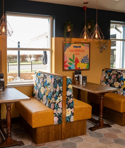 An interior restaurant seating area of The Kittoch, with upholstered booth seats, and framed artwork on the wall.