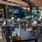 The paved, exterior beer garden seating area at The Ship; with a large wooden pergola sheltering the tables and chairs, flower baskets and string lights hanging from the dark wooden beams, and a TV on the wall.