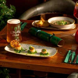 A wooden table, decorated with festive decoration is  holding a plate of scallops and opposite is a bowl of soup.