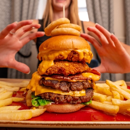 A close up image of a burger with a person in the background within the interior restaurant and seating area at a Hungry Horse venue.