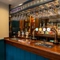 A close up view of the bar inside The Walkford in Walkford, with glasses hanging in racks above the counter, and bottles of alcoholic spirits on wooden shelves behind the bar.