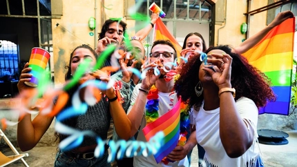 An image taken from Shutterstock of several people celebrating Pride looking at the camera with Pride Flags.