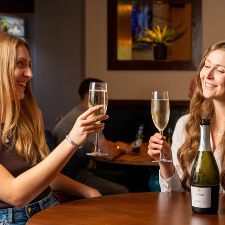 Two women seated at a restaurant table with champagne glasses and a bottle of Prosecco between them.