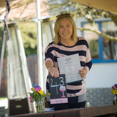 A person placing menus on tables in a beer garden, while smiling at the camera.