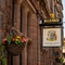 A close up view of the pub sign on the exterior wall of the Counting House. The sign features an illustration of a coat of arms held by a unicorn and a lion, above the words "Counting House, Dumbarton", on a white background.
