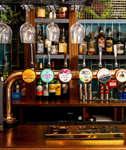 A close up view of a golden drinks tray and the beer taps for Hazy Day, Level Head, Old Mout Berries & Cherries, Inch's, San Miguel, and Birra Moretti; on the bar at The Talbot in Worcester.