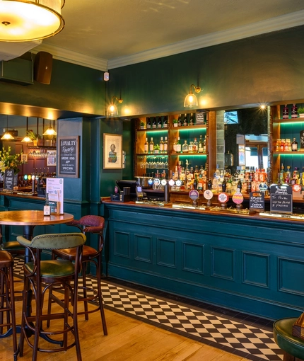 The bar and interior restaurant seating area at The Globe; with checkerboard tiles in front of the counter, TVs on the walls, and bar stool seating.