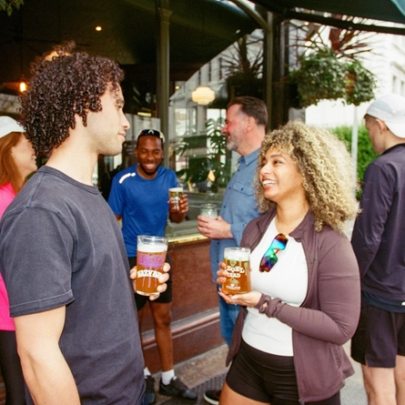 A group of friends in the exterior beer garden and seating area post marathon enjoying drinks in a Greene King London venue.