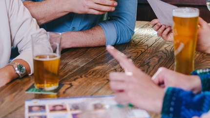 A lifestyle image of a group of friends sat at a table enjoying drinks during a Quiz event at a Greene King Pub.