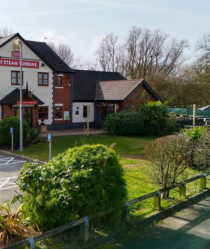 The exterior facade, signage, and beer garden seating area at The Steam Turbine in Rugby, with accessible parking spaces.