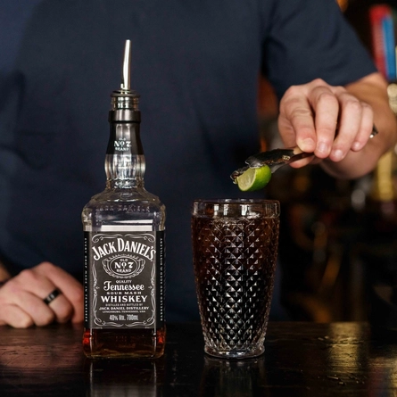 A lime wedge being dropped into a glass of Jack Daniels & Coca-Cola.