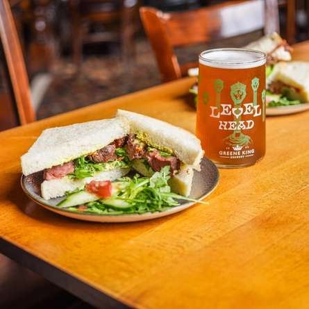 An advertising image of 2 plated sandwiches with a pint of Hazy Day and a pint of Level Head sat on an interior table for Urban Core venues.