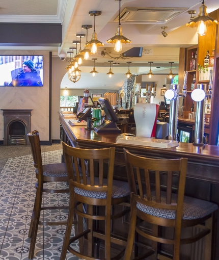 Interior bar of a pub with a seating area, a TV, a gambling machine and a fireplace.