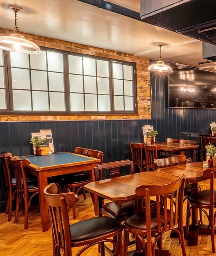 The interior restaurant seating area of the Monument, with wooden tables and chairs, booth seating, and TVs on the walls.