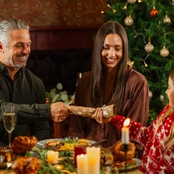 An image of 3 adults and a child pulling Christmas crackers while enjoying main dishes and drinks within the interior restaurant seating area at a Venture Hotel venue.