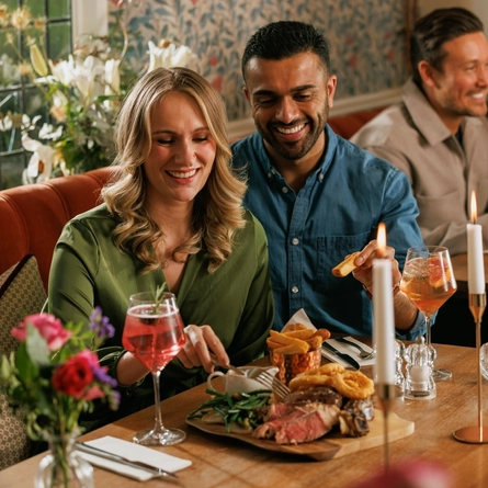 An image focusing on 2 customers enjoying a Valentines Day Ribeye Steak boarded dish sat at a table within the interior restaurant seating area of The Crown.