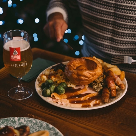 The hands of a person holding cutlery above a plated meal on a festive decorated wooden table.