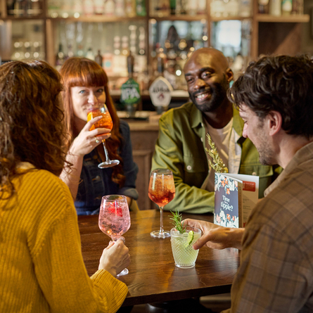 An image of 4 people sat around a table within the interior seating area enjoying cocktail style drinks at a Chef & Brewer venue.