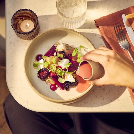 An image of sauce being poured over a bowled Warm Heritage Beetroot Salad dish from the Autumn/Winter menu available at The White Horses.