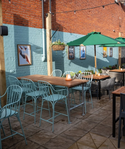 The paved, exterior beer garden seating area at The Grosvenor in Felixstowe, with shade umbrellas on some of the tables, and string lights overhead.