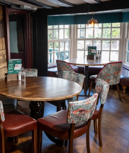 The interior restaurant seating area at The Ship in Bedford; with a large stone fireplace, upholstered bench seats in the large bay window, and wooden beams on the ceiling.
