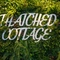 A sign on a grassy wall which reads 'Thatched Cottage'.