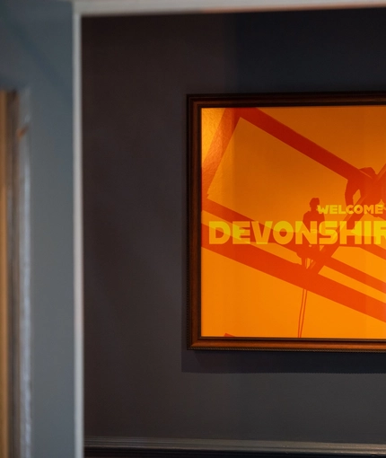 A close up view of a bright orange picture of scaffholding, featuring the words "Welcome to Devonshire Arms", on a wall inside the pub.