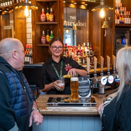 A member of staff serving two customers at the bar at The Hussey Arms.