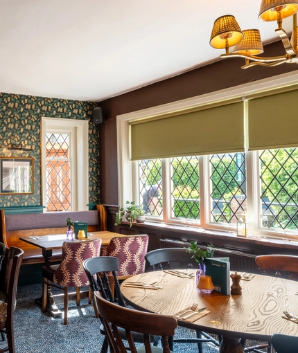 An interior restaurant seating area at The Walkford, with a padded bench seat next to the leaded windows, and a fireplace.