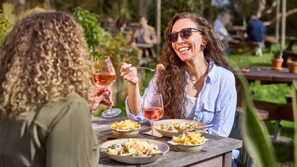 An image of 2 friends sat at a table within the exterior beer garden enjoying glasses of rose wine and bowled dishes at a Chef & Brewer venue.
