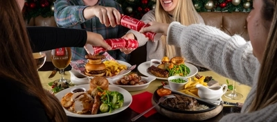 An interior shot of people celebrating Christmas and enjoying festive food in the restaurant/seating area at a Flaming Grill venue.