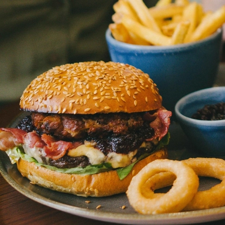 An image of 2 people celebrating with a drinks cheers while enjoying burger dishes within the interior restaurant seating area at an Urban Core venue.