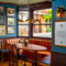An interior restaurant seating area at The London Apprentice, with a U-shaped booth seat beside the window, framed artwork on the walls, wooden flooring, and a water station.