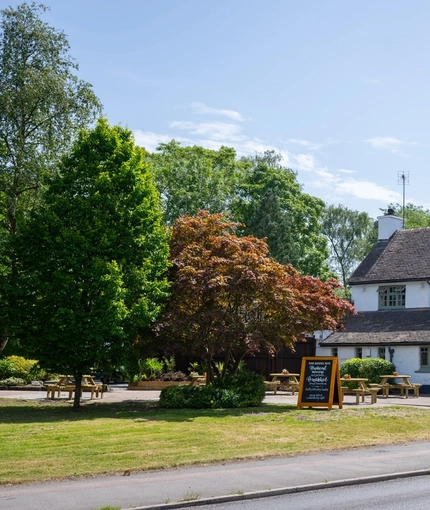 A view from across the road of the exterior facade, signage, and beer garden seating area of The Rising Sun in Wistaston.