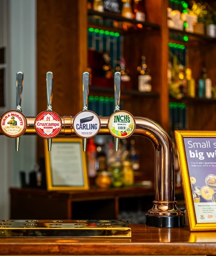 A close up view of a golden drinks tray and the beer taps for Birra Moretti, Cruzcampo, Carling, and Inch's cider, on the bar inside the Malvern Tavern.