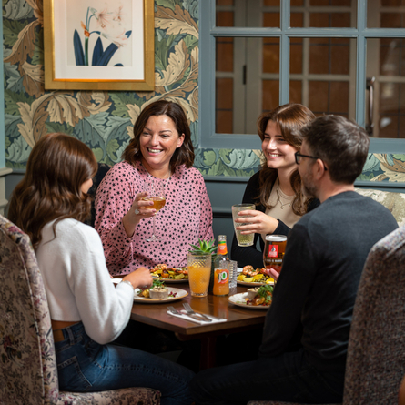 A group of people sitting around a table smiling and having a meal, with drinks in their hands.