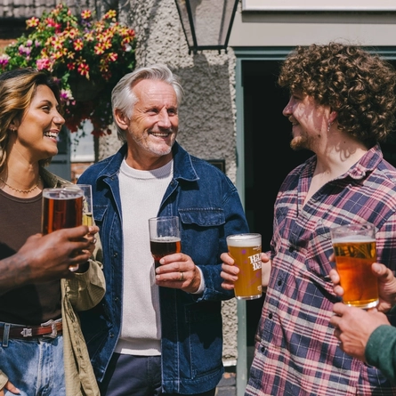 A mixed group of people stood outside a pub holding drinks.
