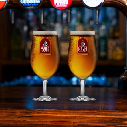 A banner showing two pints of Madri in stemmed pint glasses, standing on the bar in a pub.