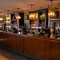 A close up view of the wood panelled bar at the Rudds Arms in Marton-In-Cleveland; with spherical lights hanging above the counter, and bottles of alcoholic spirits on illuminated wooden shelves behind the bar.